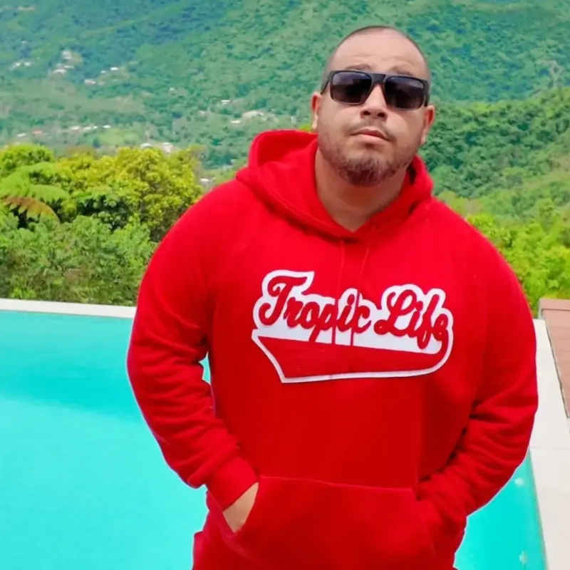 Eric of Tropic Life in a red Tropic Life hoodie beside an infinity pool in the mountains of Puerto Rico